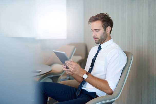 Moderno giovane uomo d'affari seduto in uno spazio ufficio contemporaneo a leggere informazioni su un tablet digitale - Foto, immagini