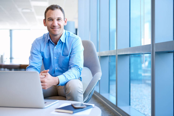 Hezký obchodní manažer středního věku sedí ve světlé moderní kanceláři a usmívá se do kamery s důvěryhodným výrazem - Fotografie, Obrázek
