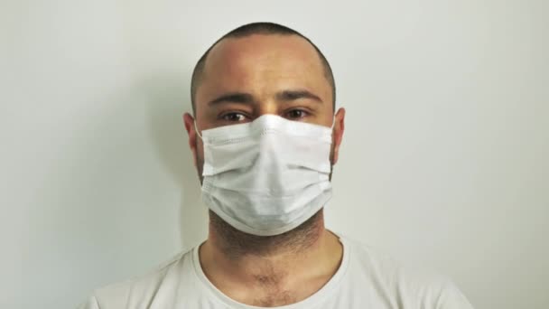 Βγάζει μια ιατρική μάσκα από το πρόσωπό του. κοντινό πλάνο σε λευκό φόντο - Πλάνα, βίντεο