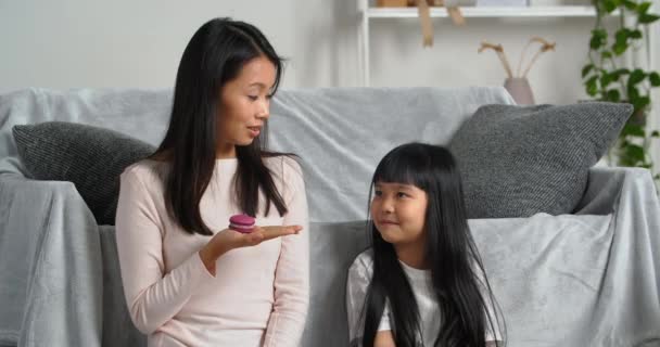 Asiatische Familie zu Hause, junge koreanische Mutter hält hausgemachte Plätzchen Backwaren Süßigkeiten in der Hand kleines Mädchen vegetarische Tochter rät, Obst zu essen zeigt Mutter grünes frisches Apfelobst, Diätkonzept - Filmmaterial, Video
