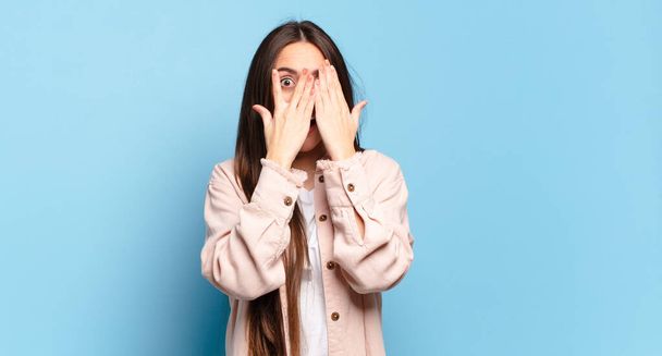 young pretty casual woman covering face with hands, peeking between fingers with surprised expression and looking to the side - Fotoğraf, Görsel