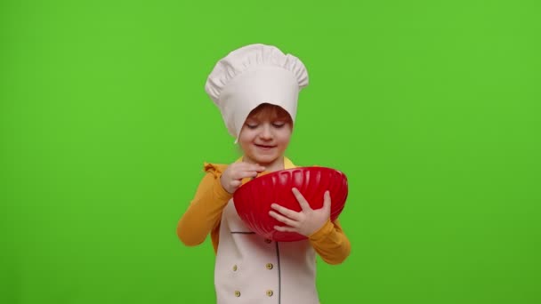 Niña vestida como cocinera cocinera mezclando masa en un tazón, preparando pan, pastel en croma key - Metraje, vídeo