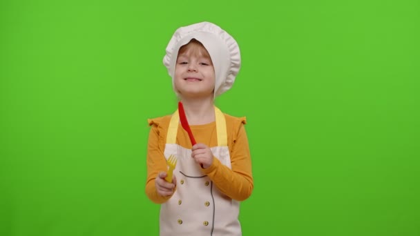 Дитяча дівчинка вдягнена кухаря пекаря в фартух і капелюсі з пластиковою вилкою і ножем, що обманює навколо
 - Кадри, відео