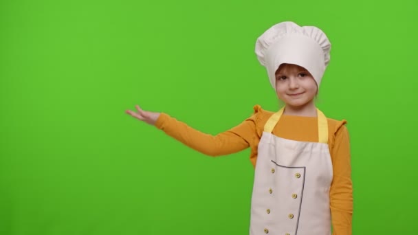 Niña vestida como chef cocinero apuntando a la izquierda en el espacio en blanco, lugar para el logotipo de su anuncio - Imágenes, Vídeo