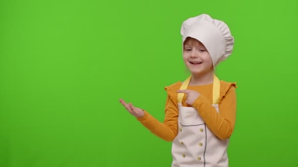 Bambino ragazza vestito cuoco cuoco panettiere in grembiule che punta a sinistra sullo spazio bianco su sfondo chiave croma - Filmati, video