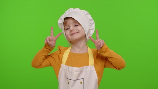 Маленькая девочка, одетая как повар, показывает знак победы, надеясь на успех и победу, мир - Кадры, видео