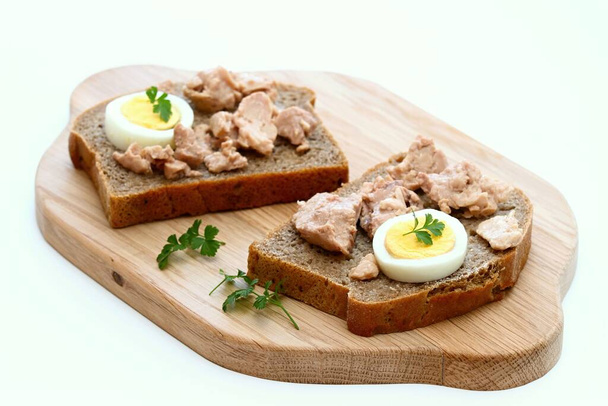 Tresčí játra a vejce na hnědém chlebu s petrželkou. Zdravý sendvič na řezacím prkně. Přírodní zdroj vitamínu D a omega 3, bílé pozadí. - Fotografie, Obrázek