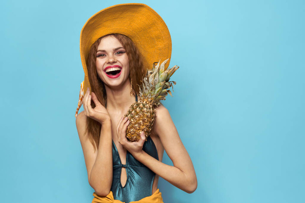 kobieta w kapelusz plażowy ananas gospodarstwa strój kąpielowy egzotyczne owoce niebieski tło wakacje - Zdjęcie, obraz