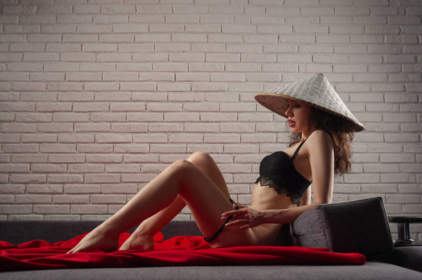 sottile sexy donna prende off il suo biancheria intima e asiatico cappello su il divano - Foto, immagini