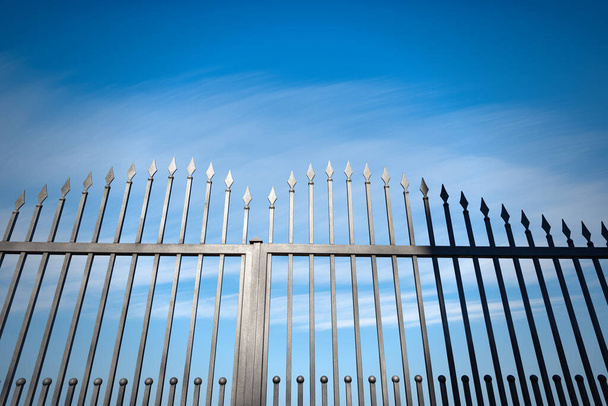 Closeup of a wrought iron gate with sharp points on blue sky with clouds and copy space. - Photo, Image