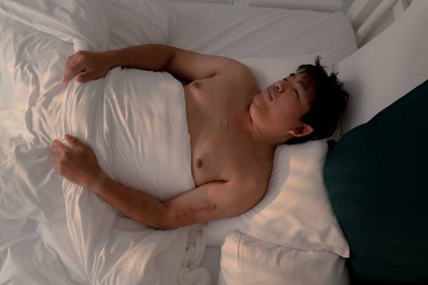 παχουλός Ασιάτης κοιμάται στο λευκό κρεβάτι με χαρούμενο πρόσωπο το πρωί, καλό όνειρο, τεμπέλικη μέρα - Φωτογραφία, εικόνα