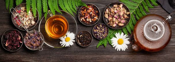 Różne ziołowe sucha herbata, czajnik i filiżanka na drewnianym stole. Widok z góry płaski lay - Zdjęcie, obraz