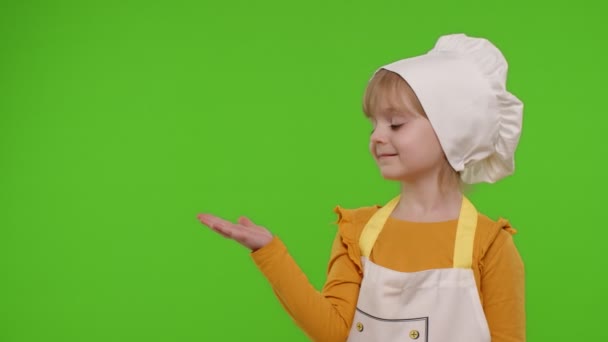 Παιδί κορίτσι ντυμένος σαν σεφ μάγειρας δείχνοντας αριστερά στο κενό χώρο, θέση για το λογότυπο διαφήμισή σας - Πλάνα, βίντεο