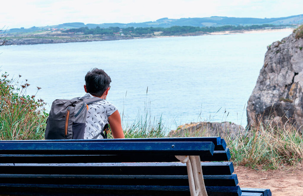 kobieta z plecakiem siedząca na ławce i patrząca na morze - Zdjęcie, obraz