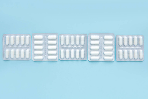 Envases de blister de píldoras blancas sobre fondo azul, vista superior. Diferentes medicamentos, comprimidos, cápsulas de medicamentos. Concepto de medicina. - Foto, Imagen