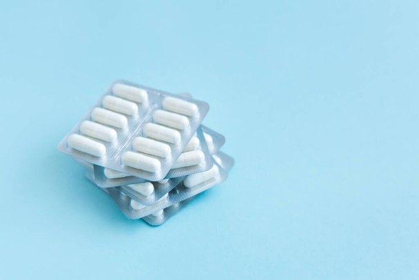 Packs of white pills on blue background. Tablets, capsules with medicines for headache and toothache. Pain reliever. Treatment concept. Copy space. - Photo, Image