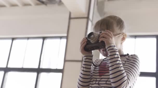 Nuori tyttö oppii ottamaan kuvia vanhanaikaisella kameralla. Toimintaa. Pieni tyttö pitelee kameraa valokuva tai video studio. - Materiaali, video