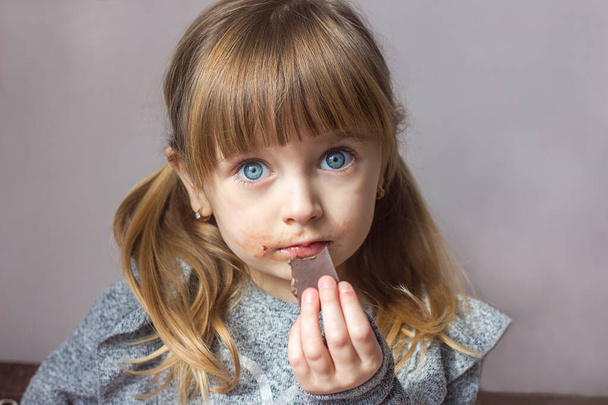 Petite fille au chocolat à la main portrait flou gros plan, émotions enfantines enfance heureuse, mal des bonbons pour les dents, mise au point sélective - Photo, image