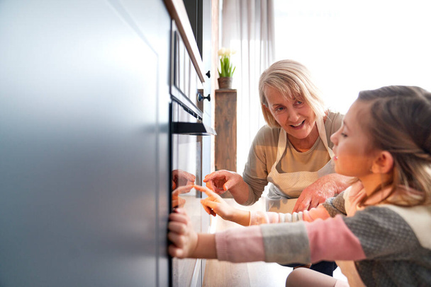 Ragazza e nonna guardando biscotti pasquali nel forno della cucina - Foto, immagini