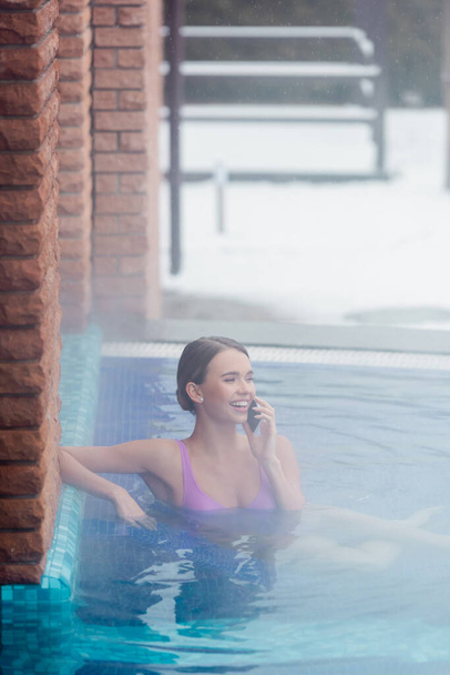 外の温泉に浸かりながらスマホで話す水着姿の幸せな女性 - 写真・画像