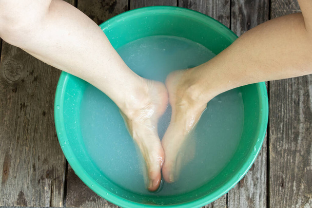 the girl washes her feet in a green bowl on the floor of the house - Photo, Image