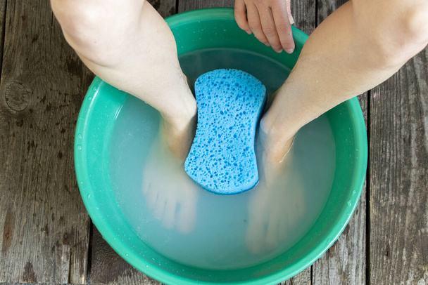 the girl washes her feet in a green bowl on the floor of the house - Photo, Image