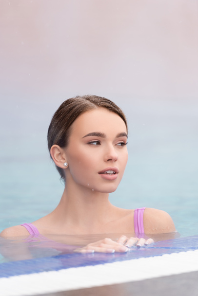 屋外の温泉プールで泳いでいる若い女性の近くの蒸気  - 写真・画像