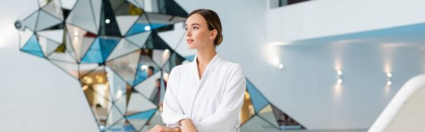 Nuori nainen valkoisessa kylpytakissa katselee pois kylpyläkeskuksessa, banneri - Valokuva, kuva