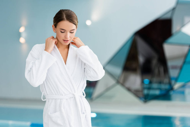 mujer joven ajustando el albornoz blanco en el centro de spa  - Foto, imagen