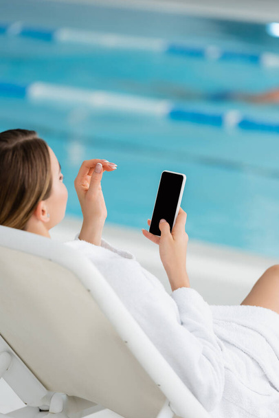 young woman resting on deck chair and holding smartphone with blank screen  - Foto, afbeelding