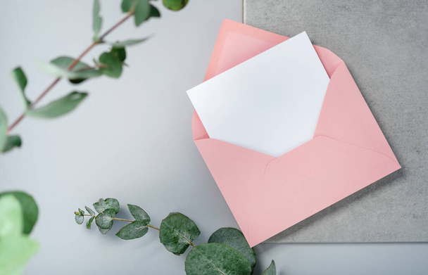 Une vraie photo. Carte d'invitation carrée enveloppe rose avec une branche d'eucalyptus. Vue du dessus avec espace de copie, fond gris clair. Modèle de marque et de publicité - Photo, image