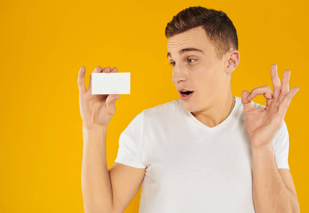 A guy in a white t-shirt shows a credit card on a yellow background cropped view - Foto, Bild