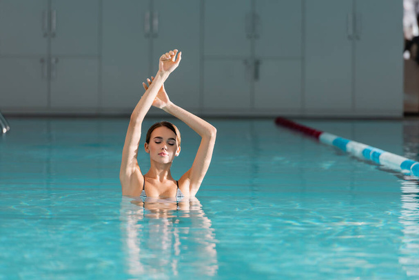 νεαρή γυναίκα με υψωμένα χέρια που κολυμπούν στην πισίνα του κέντρου σπα πολυτελείας  - Φωτογραφία, εικόνα