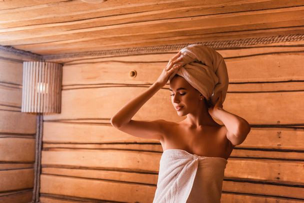 Młoda kobieta mocuje ręcznik na głowie w saunie  - Zdjęcie, obraz