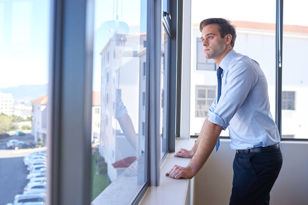 Красивий молодий бізнес-підприємець стоїть у великих вікнах свого офісу і дивиться на погляд з вдумливим виразом
 - Фото, зображення