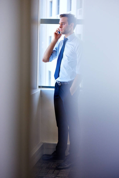 Красивий молодий корпоративний працівник стоїть в сучасному офісі поруч з великим вікном, розмовляючи на мобільному телефоні
 - Фото, зображення