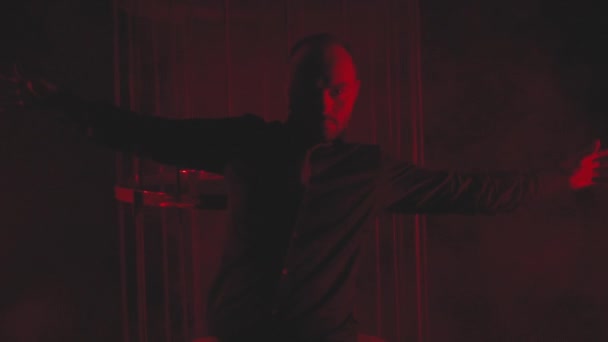 Man in zwart in rood licht in rook bij de metalen kooi - Video