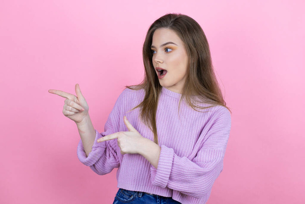 Jonge mooie vrouw met lang haar staan over geïsoleerde roze achtergrond verrast en wijzen haar vingers kant - Foto, afbeelding