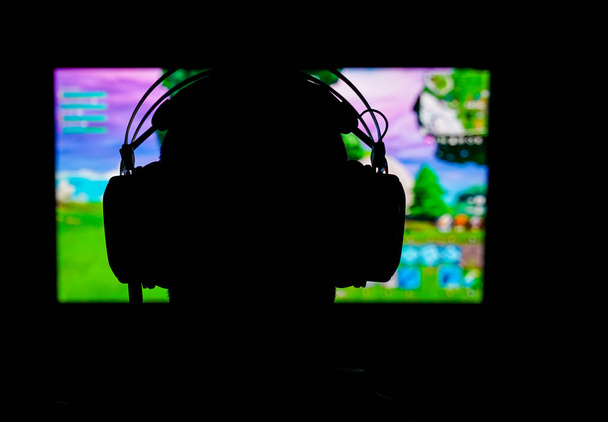 Silhouette of a young gamer wearing a headset while playing a popular battle royale game. Blurred background. High quality photo - Photo, Image