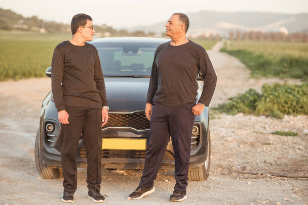Elderly father and young son standing next to car in nature on road trip. - Photo, Image
