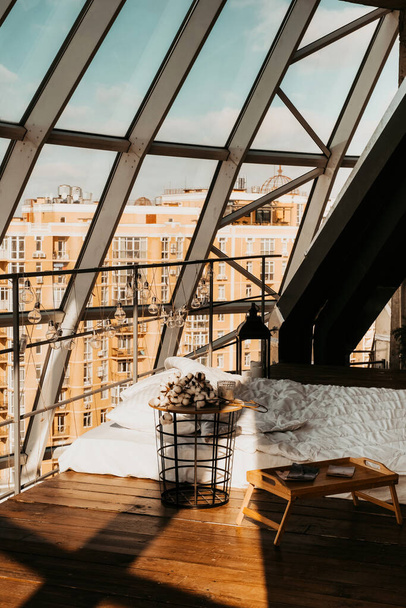 ylellinen kattohuoneisto lasikatto näköalalla kaupunkiin. sänky valkoiset liinavaatteet parvi tyyli makuuhuoneessa. Nykyaikaiset huoneistot - Valokuva, kuva