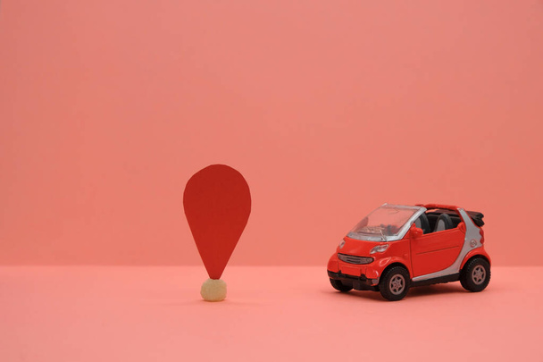 Red small car toy near the location sign. Travel or delivery concept. Car services. Coral background. Copy space. - Photo, Image