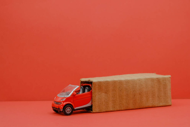 Rood klein autootje bij de uitgepakte doos. Auto winkelen concept. Kopieerruimte. - Foto, afbeelding