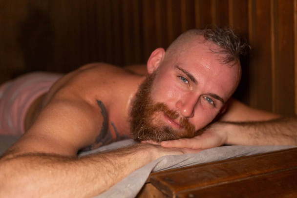 Portrait d'un homme brutal avec une casquette de barbe sur la tête se trouve dans un sauna spa, processus de nettoyage de bien-être - Photo, image