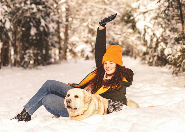 Mladá usměvavá dívka s bílým psem Labrador hraje se sněhem v zimním lese - Fotografie, Obrázek