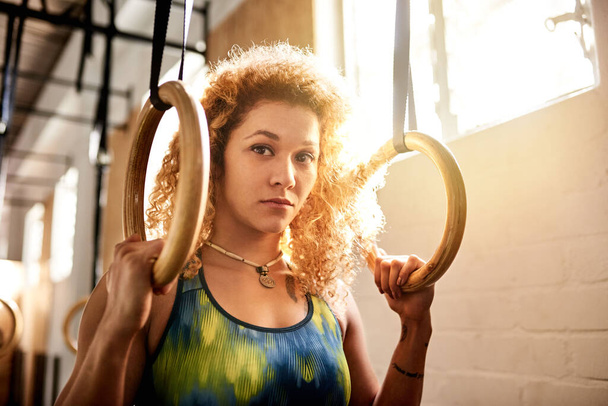 Fit jovem mulher olhando focado enquanto exercitando-se em anéis durante uma sessão de treino sozinho no ginásio - Foto, Imagem