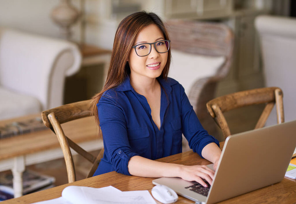 Ritratto di una giovane imprenditrice asiatica sorridente seduta a casa con gli occhiali che lavora online con un computer portatile  - Foto, immagini