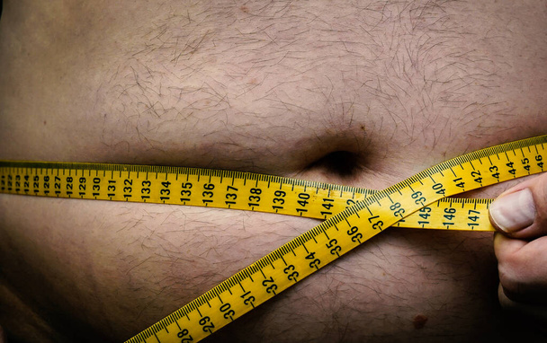 Misurazione del nastro su una pancia maschile grassa sovrappeso. Chiudete. Foto di alta qualità - Foto, immagini