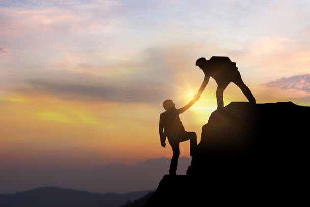 Business team success concept.silhouette of business man on peak mountain climbing helping on sunset background teamwork - Photo, Image