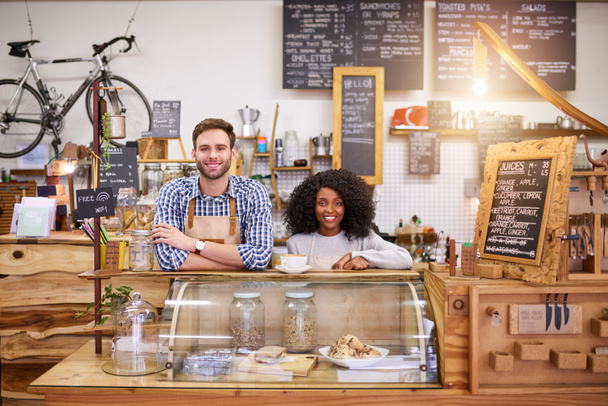 Portrait de deux jeunes baristas souriants, debout ensemble derrière le comptoir d'un café branché - Photo, image